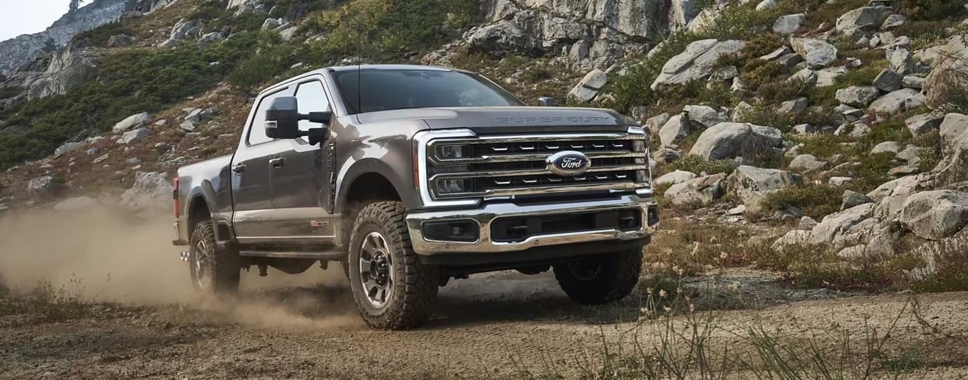 A grey 2023 Ford F-250 is shown driving on a remote dusty dirt road.