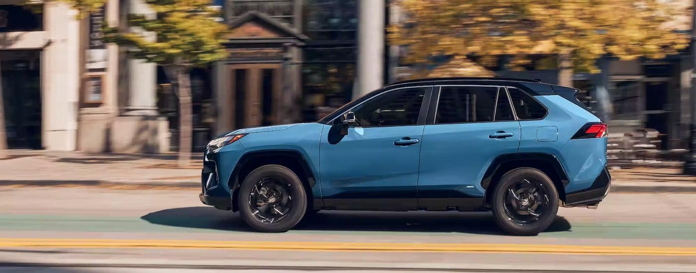 A blue 2023 Toyota RAV4 XSE Hybrid is shown from the side driving on a city street.
