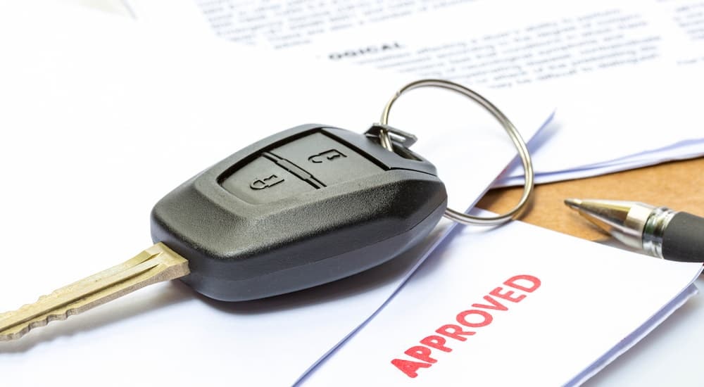 A close up of a car key on top of approved loan paperwork is shown.