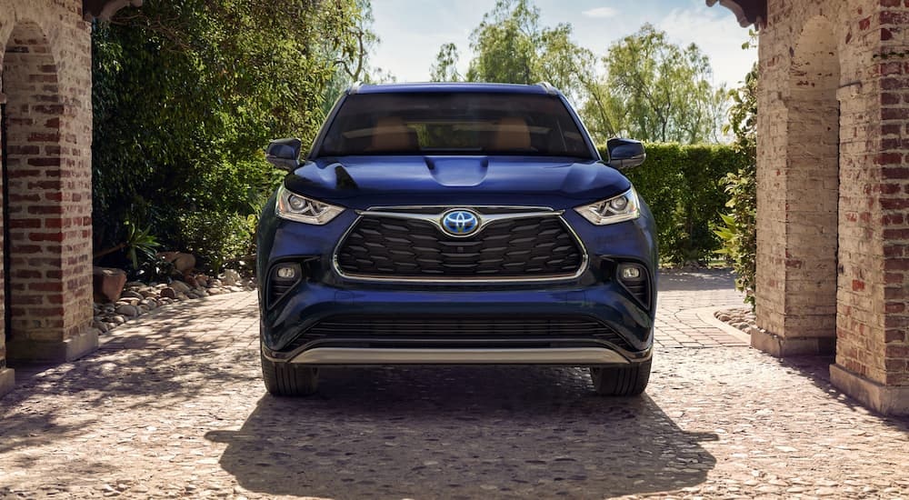 A dark blue 2023 Toyota Highlander Hybrid is shown from the front parked beneath a stone archway.