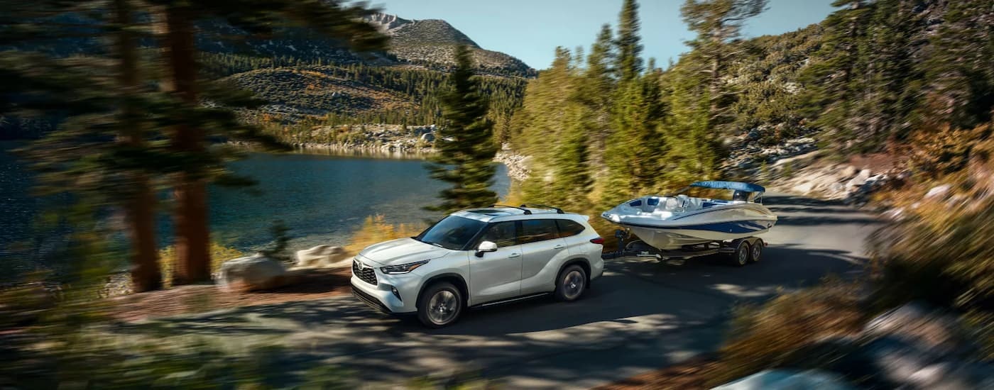 A white 2022 Toyota Highlander XLE is shown towing a small boat next to a lake.
