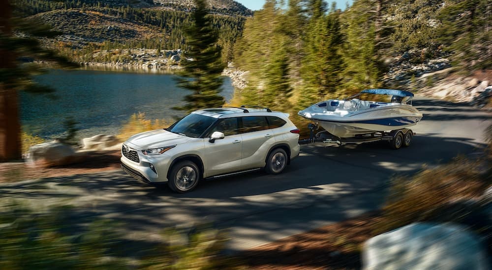 A white 2020 Toyota Highlander is shown towing a boat next to a lake.
