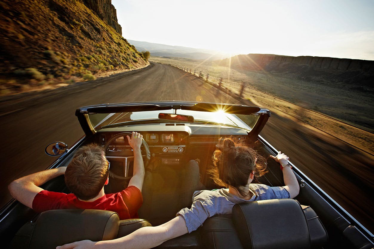 a couple driving down a highway in a top drop car