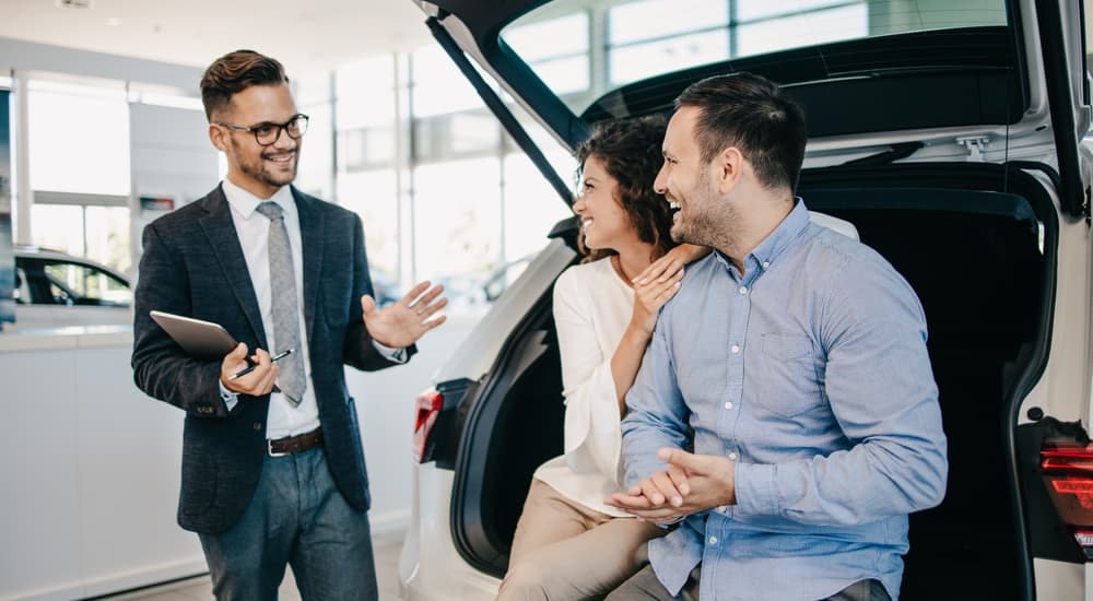 A salesman is shown speaking to a couple inside of a car dealership.