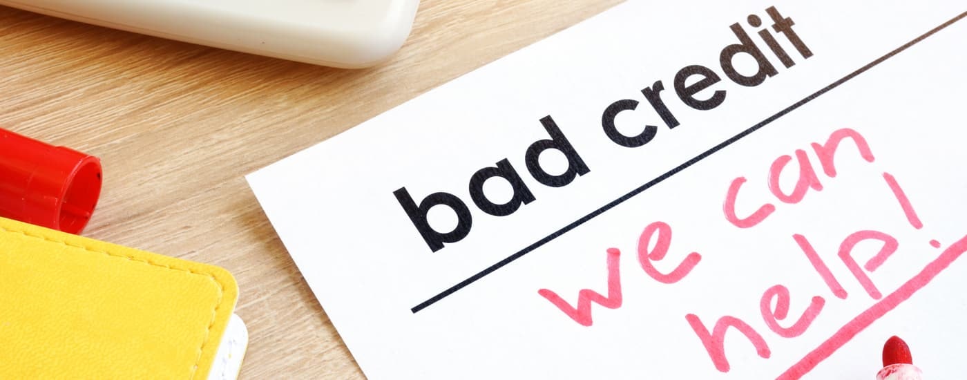 A piece of paper that says 'bad credit we can help' is shown on a desk.