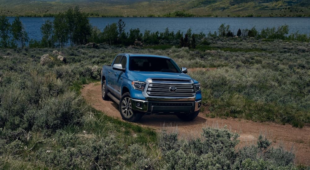 A blue 2021 Toyota Tundra Limited is shown driving on a dirt road near a lake.