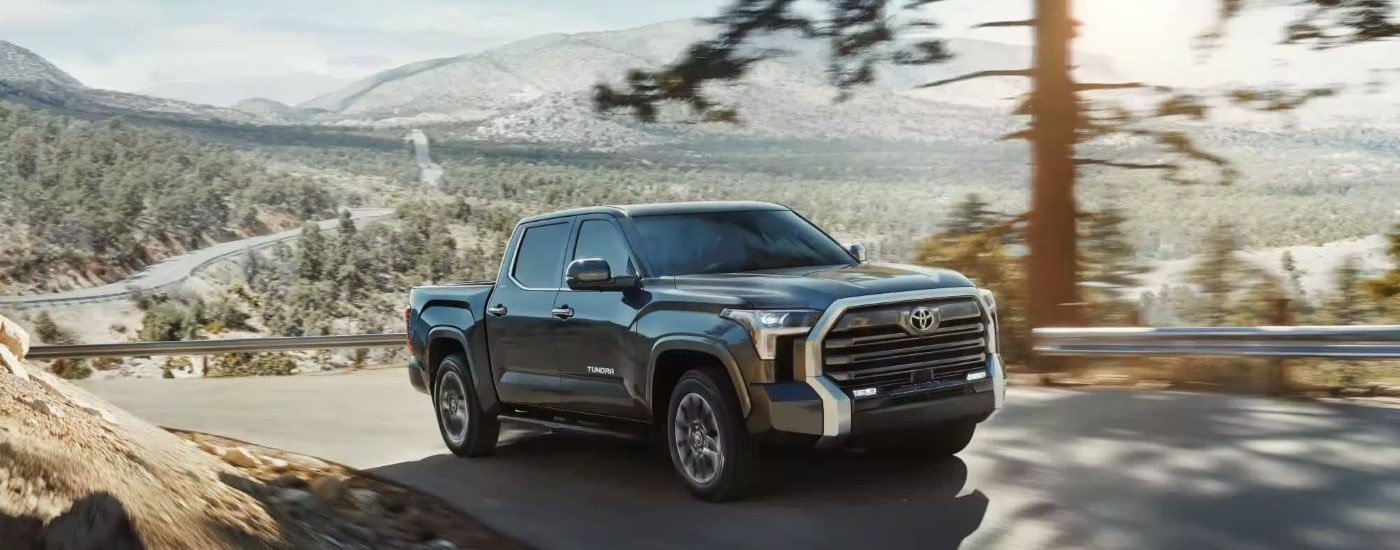 A black 2023 Toyota Tundra Limited is shown driving on a tree-lined road.