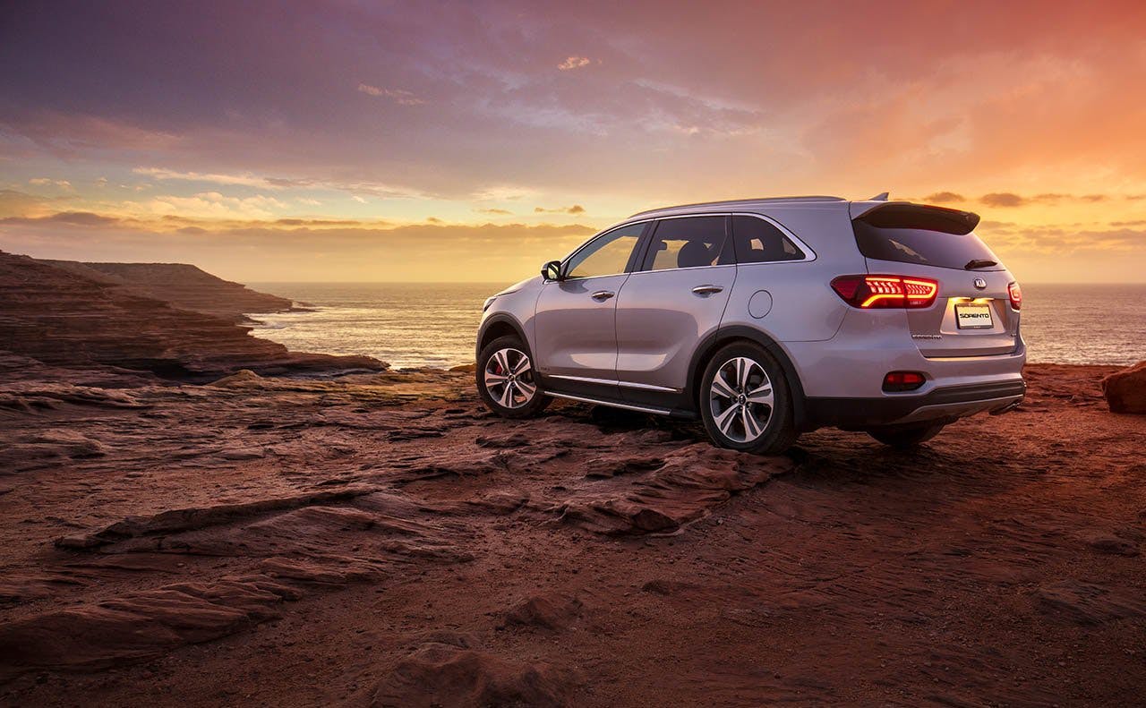 a silver kia SUV parked on a clear viewing the ocean