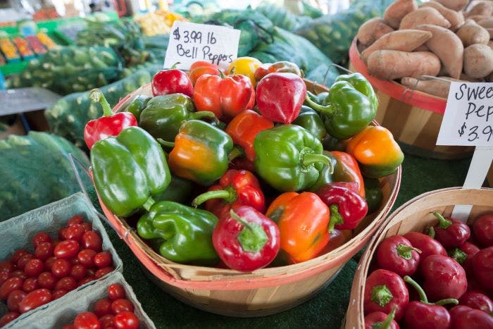 Bell peppers, sweet red peppers, sweet potatoes, and cherry tomatoes on display at local farmers market