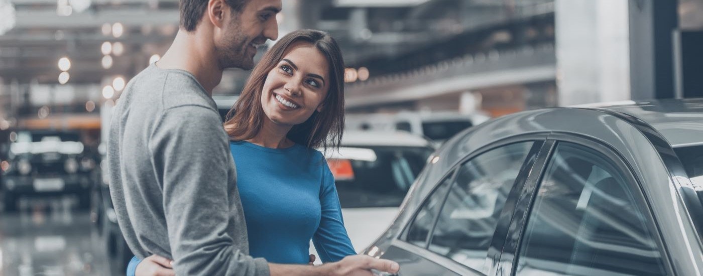 A smiling couple is shown at a dealership after going to 'sell my car.'