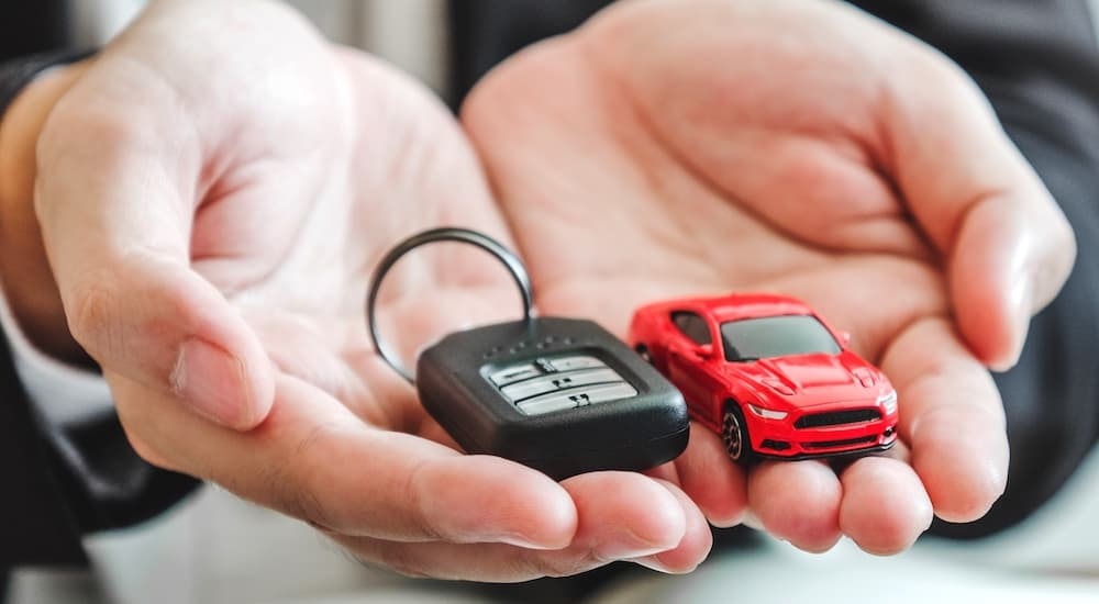 Hands are shown holding a toy car and key fob during the 'sell my car' process.