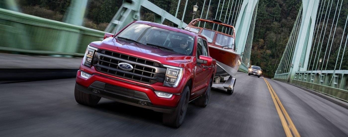 A red 2021 Ford F-150 is shown towing a boat over a bridge.