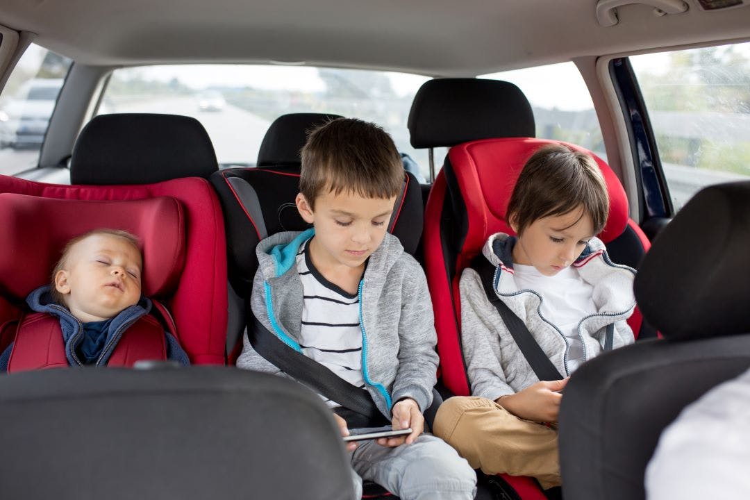 three children in the back seat of a car, inside a car seat