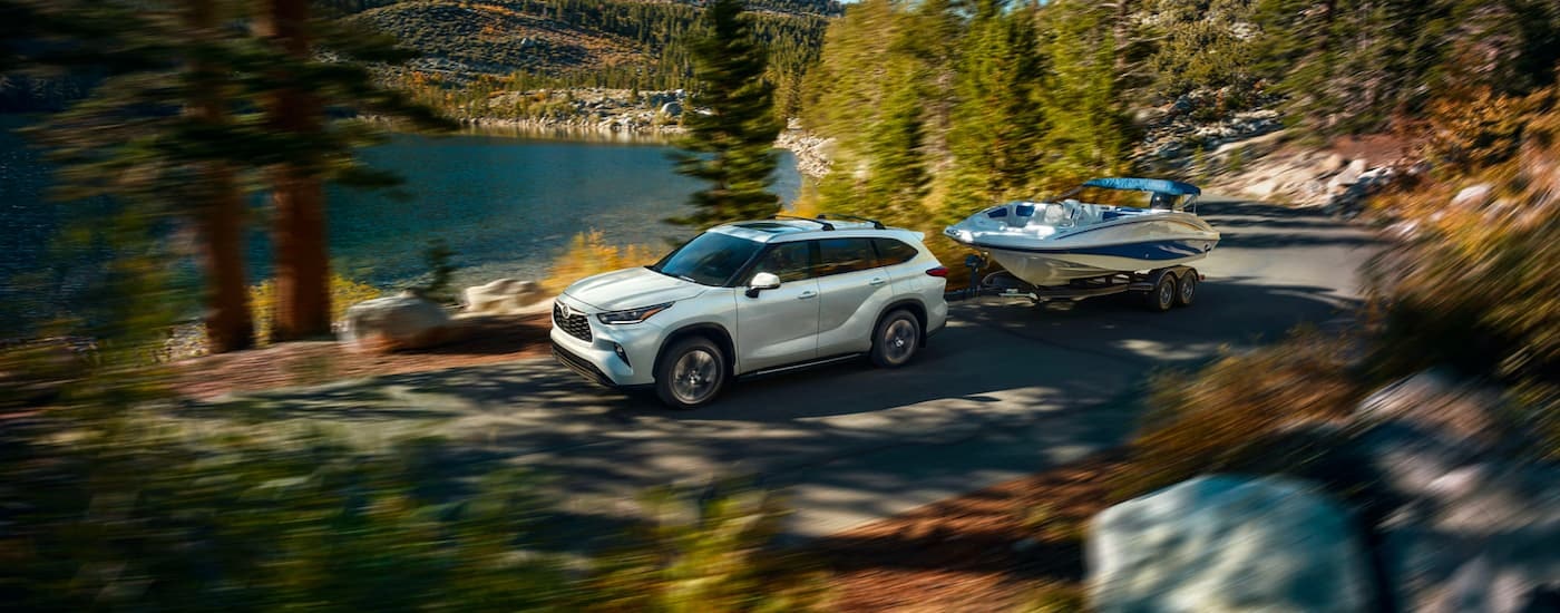A white 2023 Toyota Highlander XLE is shown towing a boat past a lake.