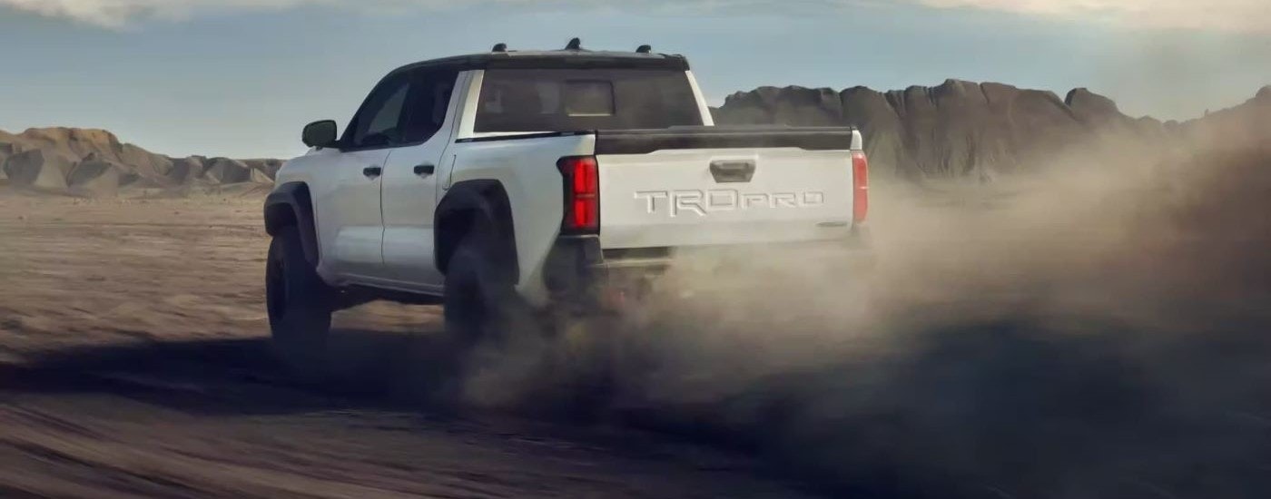A white 2024 Toyota Tacoma TRD Pro is shown from the rear kicking up dust.