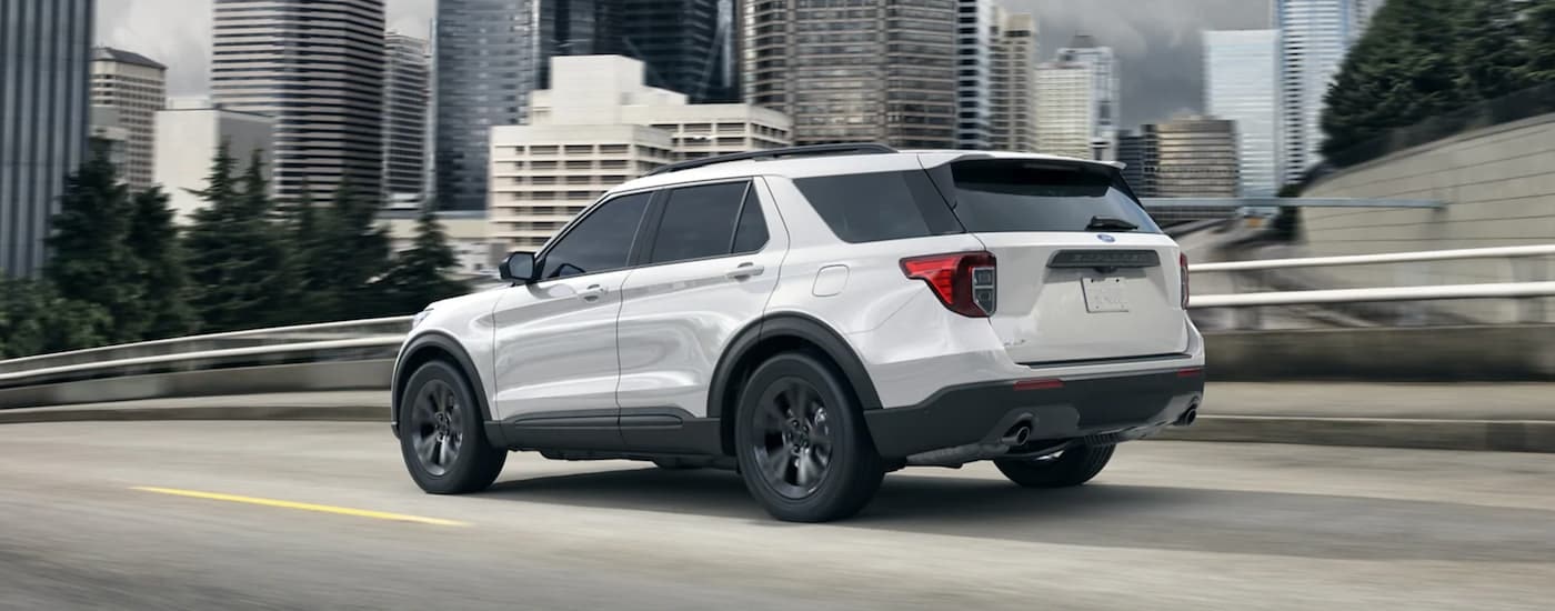 A white 2021 Ford Explorer is shown driving past city buildings.