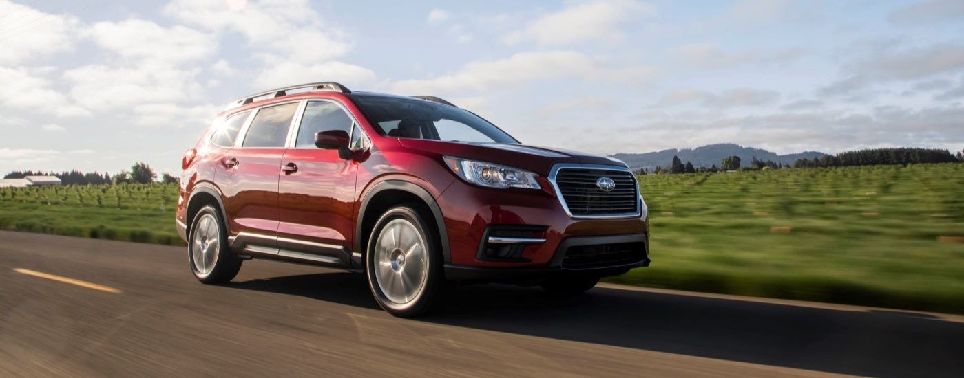 A red 2019 Subaru Ascent Limited is shown driving past a field.