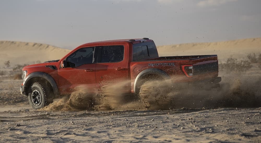 A red 2021 Ford F-150 Raptor is shown from the side while off-road.