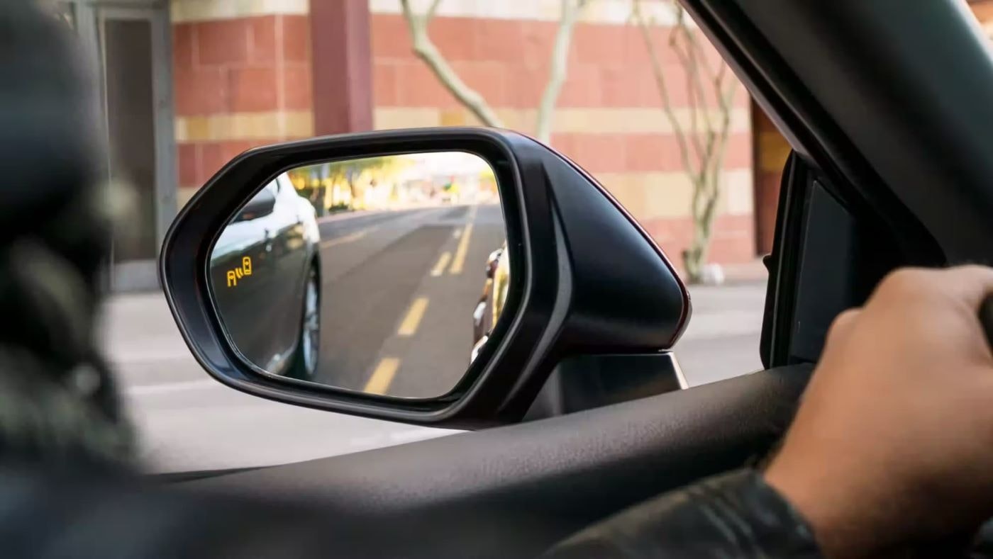 A close up shows the blind spot monitoring icon on the mirror of a red 2023 Toyota Camry.