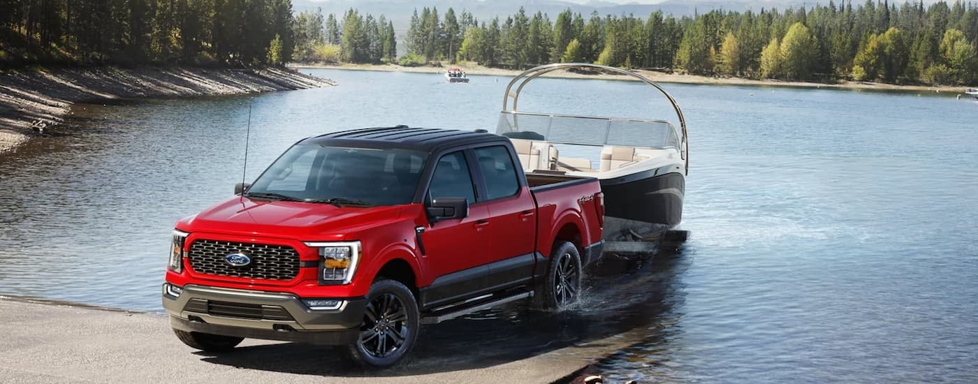 A red 2023 Ford F-150 Heritage Edition is shown towing a boat out of a lake.
