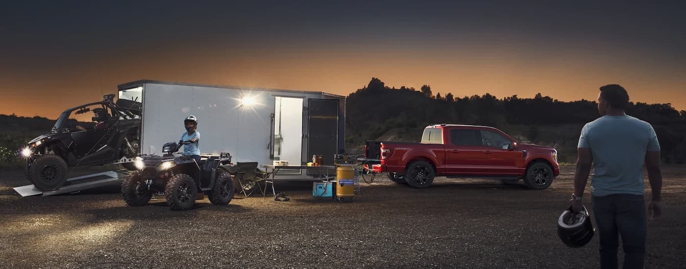 A group of people with UTVs are shown next to a red 2023 Ford F-150 by a trailer.