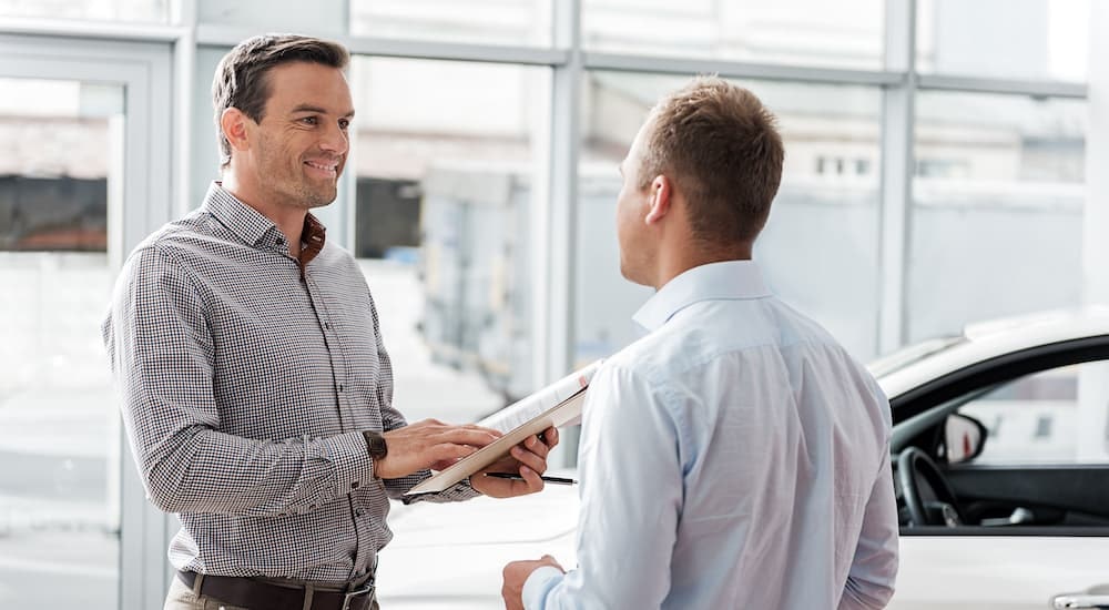 Two people are shown talking at a car dealership.