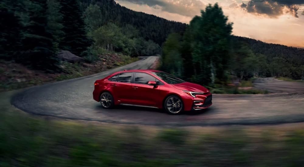 A red 2023 Toyota Corolla is shown from the side while rounding a bend.