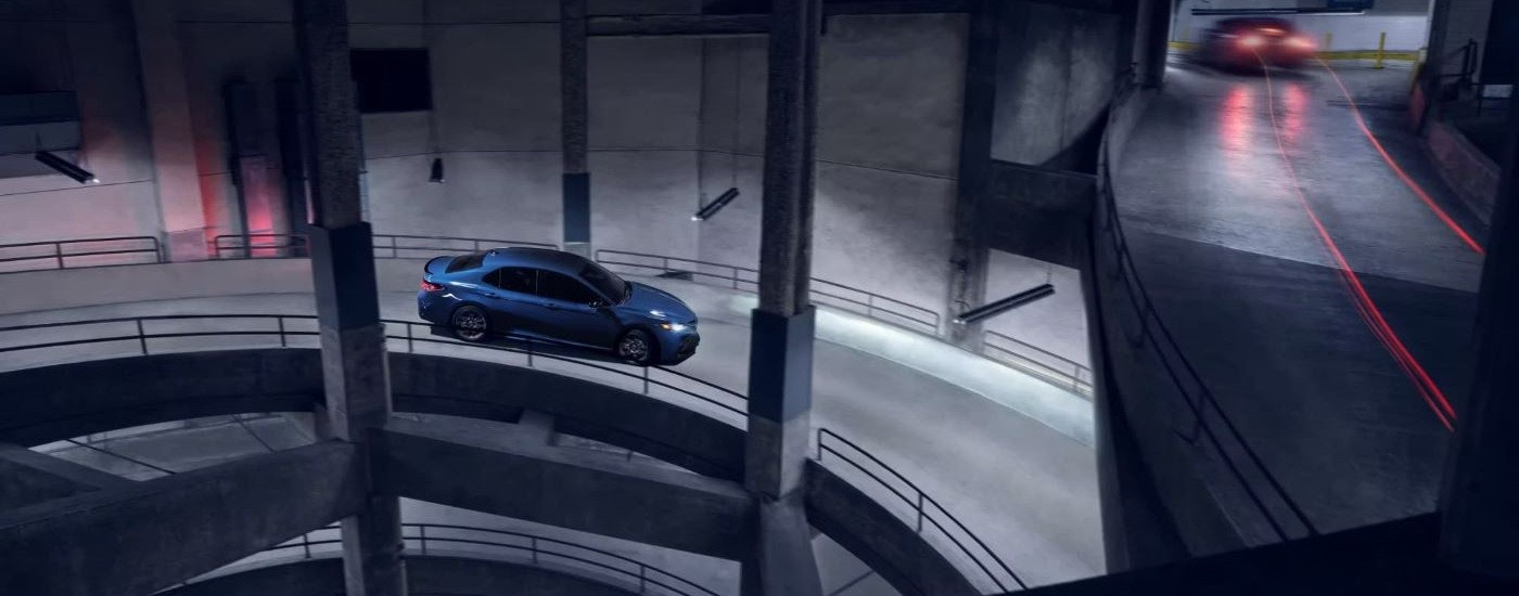 A blue 2024 Toyota Camry Nightshade Edition is shown on a ramp in a parking garage.