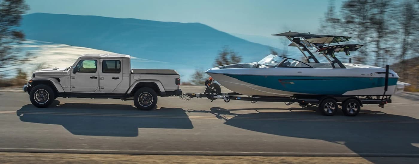 A silver 2023 Jeep Gladiator is shown from the side while towing a boat.