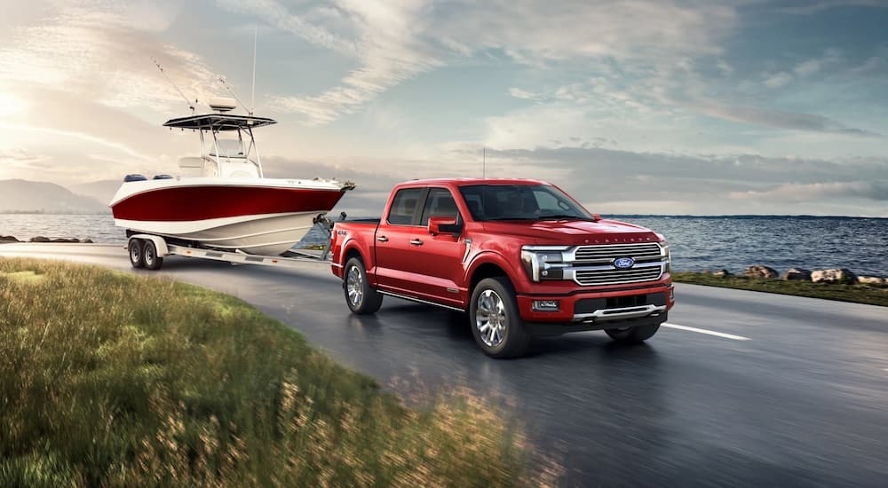 A red 2024 Ford F-150 Platinum Plus is shown from the front at an angle while towing a boat.
