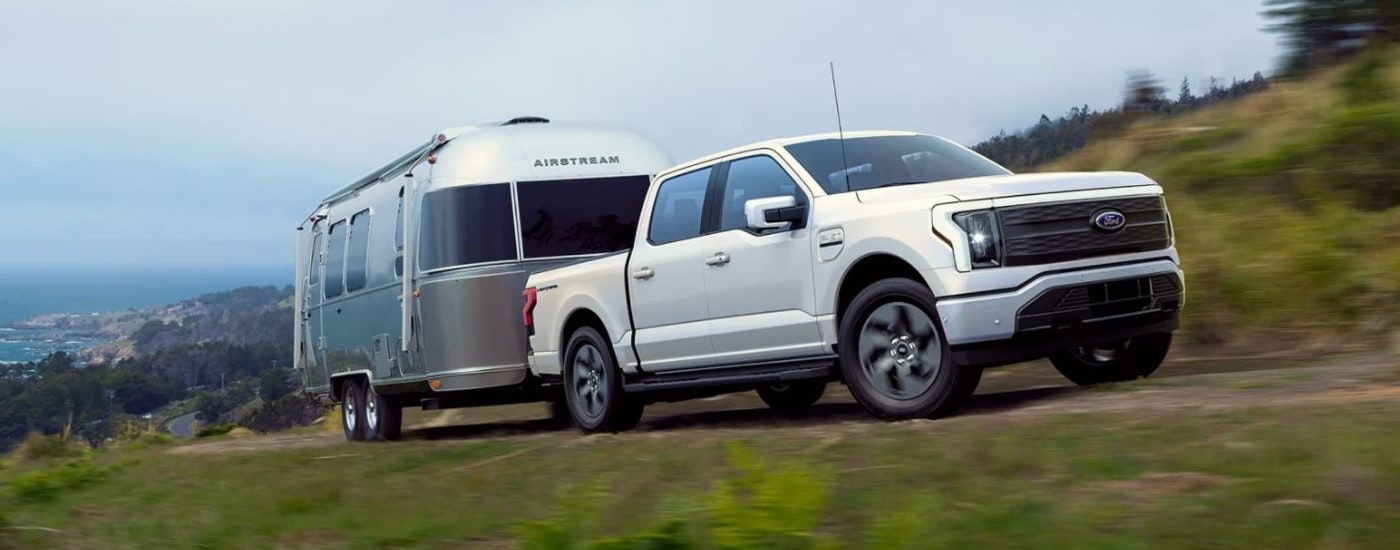 A white 2023 Ford F-150 Lightning is shown towing an Airstream trailer.