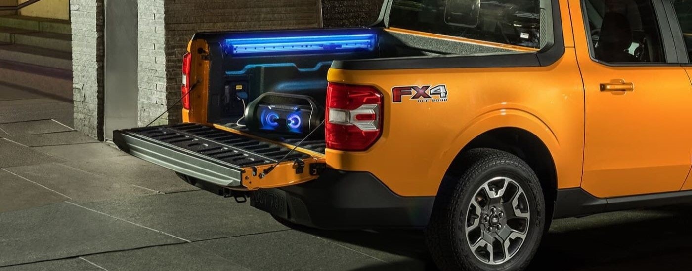 A boombox and accent lighting are shown in the bed of a yellow 2024 Ford Maverick.