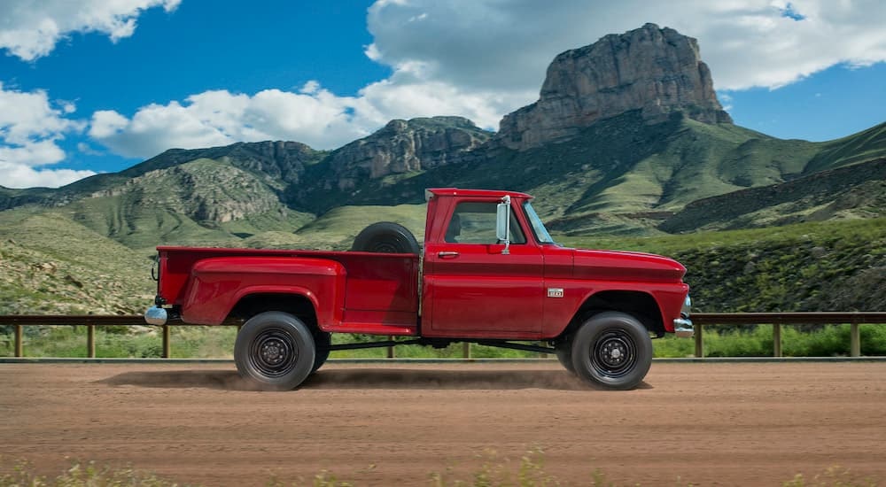 A red 1960 Chevy C/K is shown from the side on a dirt road.