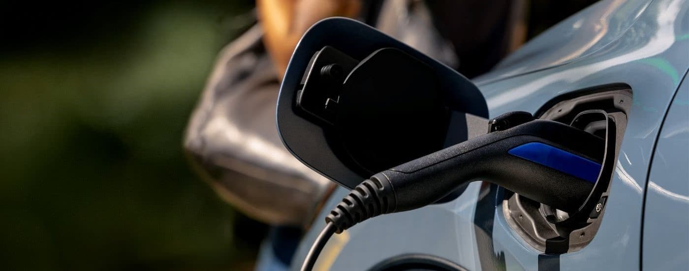 A close up shows the plug charging a blue 2023 Ford Escape Hybrid.