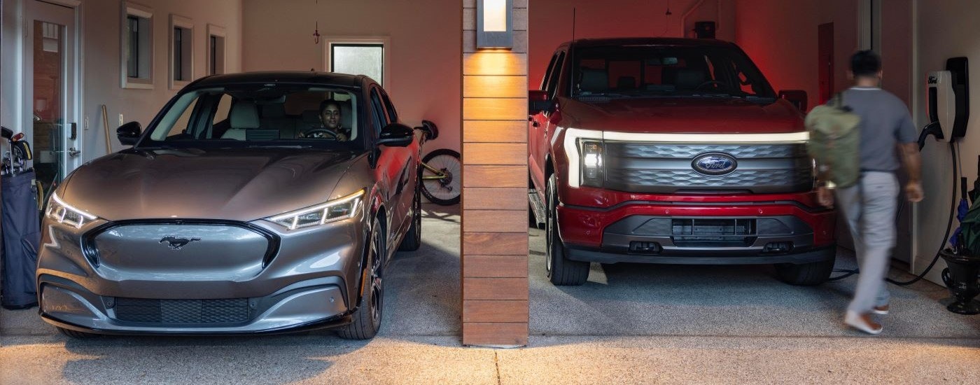 A grey 2023 Ford Mustang Mach-E and a red F-150 Lightning are shown in a garage.