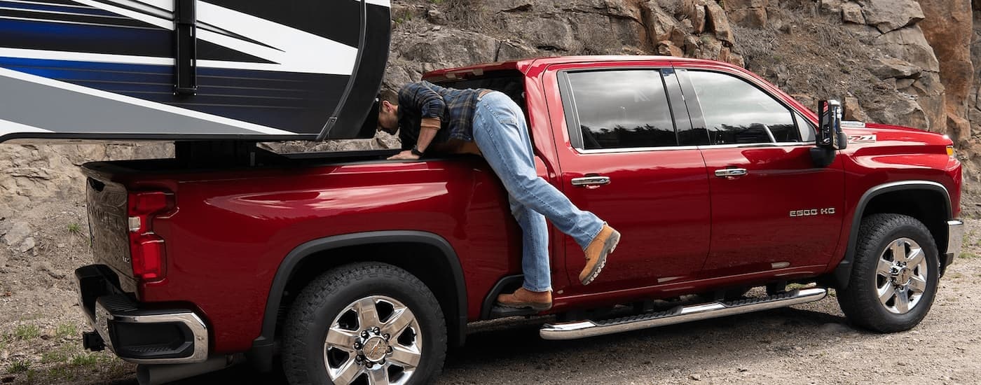 A man is shown leaning into the bed of a red 2022 Chevy Silverado 2500HD Z71 that's towing a camper.