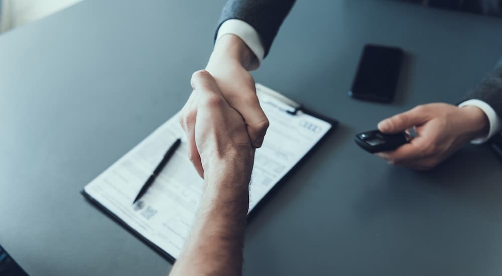 Two people are shown shaking hands over financing paperwork.