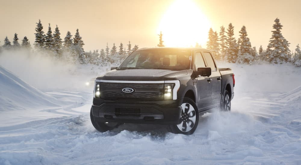 A black 2022 Ford F-150 Lightning is shown from the front at an angle in the snow after leaving a Ford F-150 Lightning dealer.