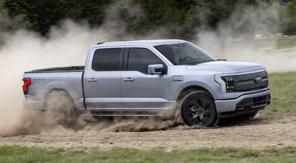 A silver 2023 Ford F-150 Lightning Lariat is shown from the side on a dirt trail.