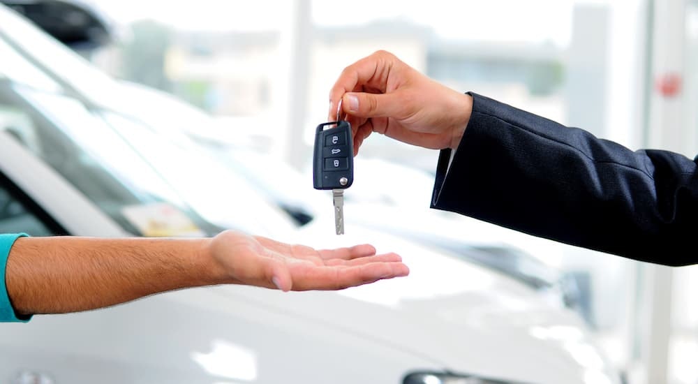 A car key is shown exchanging hands at a dealership.