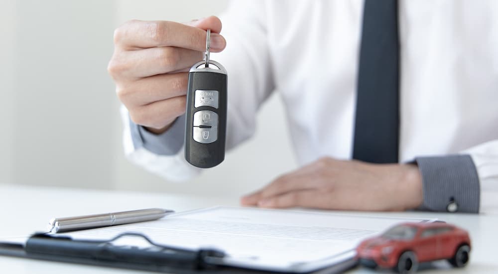 A salesman is shown holding a key fob over financing paperwork.