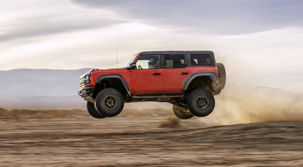 An orange 2024 Ford Bronco Raptor is shown from the side while jumping through the air after leaving a Ford Bronco dealer..