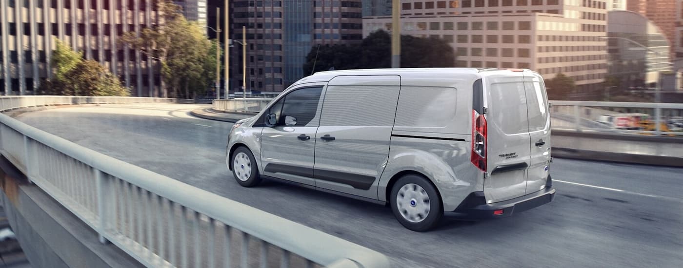 A grey 2023 Ford Transit Connect XLT is shown from a rear angle driving on a city bridge.