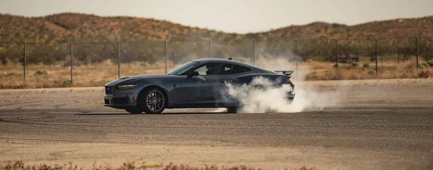 A dark grey 2024 Ford Mustang Dark Horse is shown kicking up smoke on pavement.