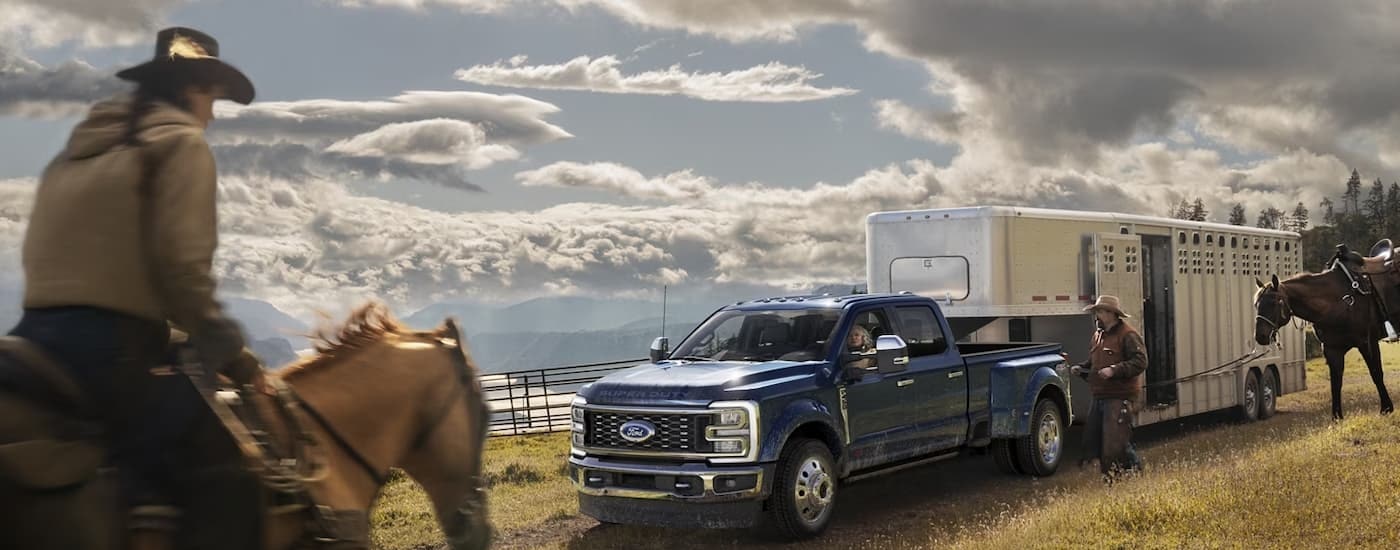 A blue 2024 Ford Super Duty F-450 is shown on a farm towing a silver horse trailer.