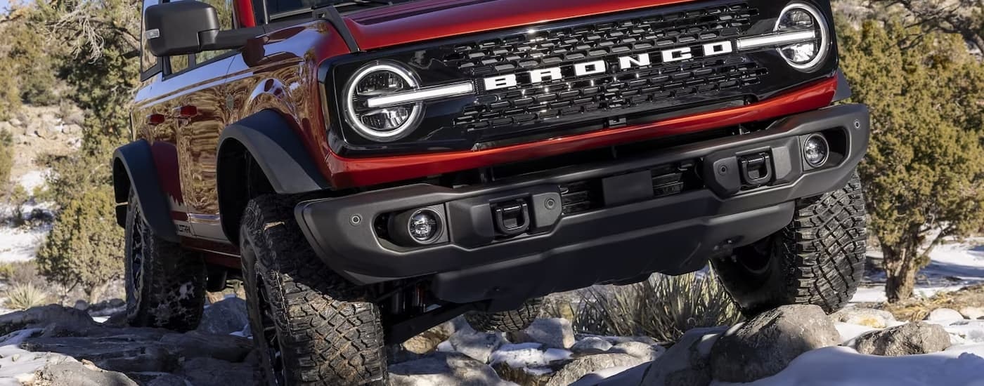 A red 2024 Ford Bronco Wildtrak is shown off-roading on a snowy path.