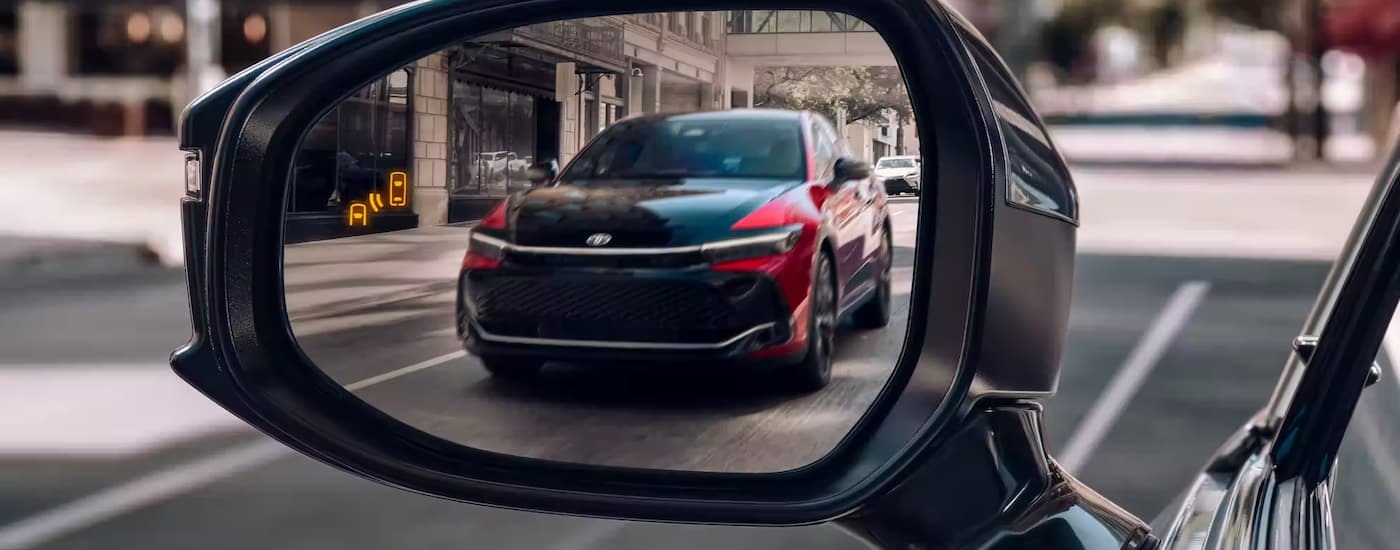 A black and red 2023 Toyota Crown is shown in the side mirror of a vehicle on a city street.