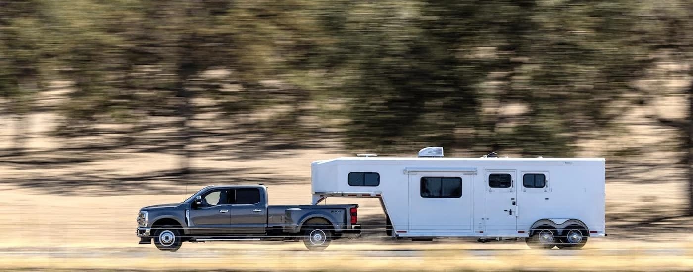 A grey 2023 Ford F-350 is shown from the side while towing a camper after leaving a used Ford truck dealer..