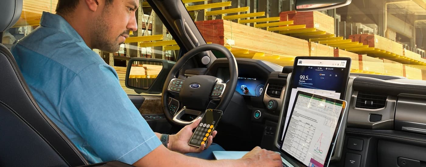 A person is shown using a laptop and smartphone in a 2024 Ford F-150 Lightning.
