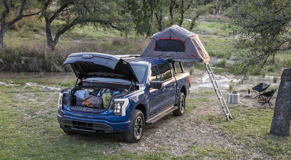 A blue 2024 Ford F-150 Lightning XLT is shown from the front at an angle while powering a campsite.